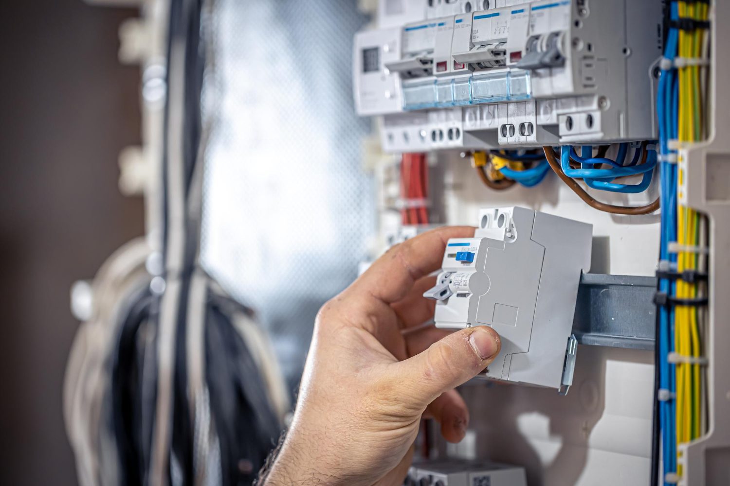 A male electrician works in a switchboard with an electrical connecting cable A male electrician works in a switchboard with an electrical connecting cable<br />